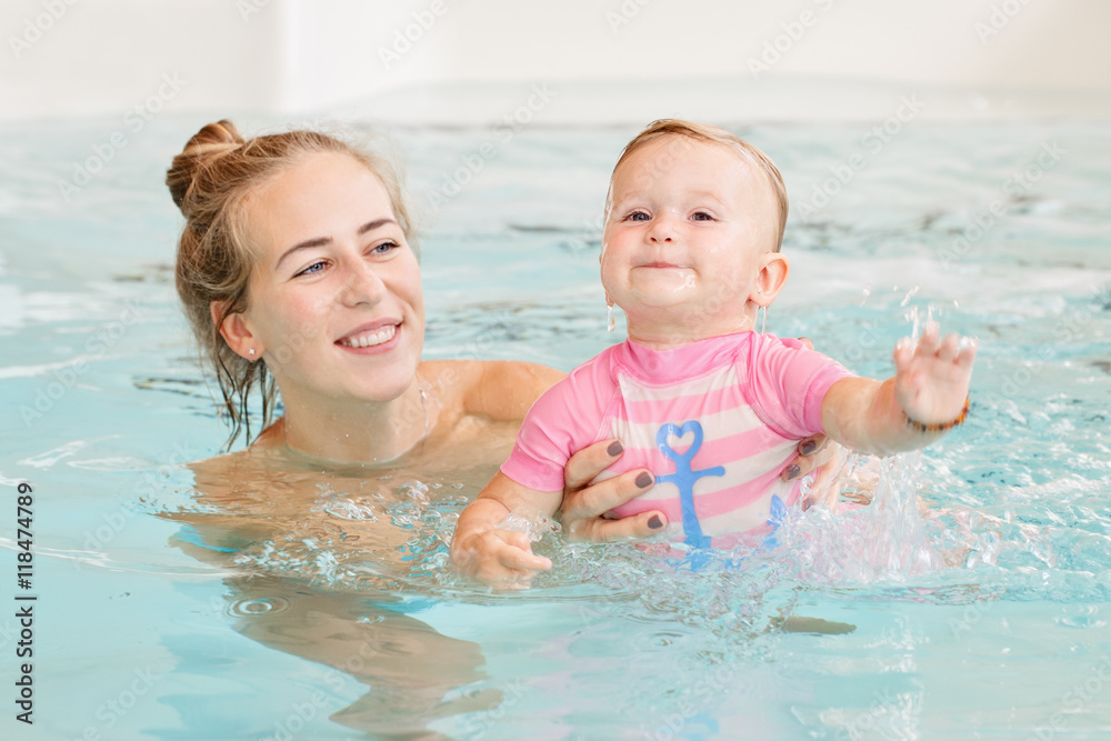Group portrait of white Caucasian mother and baby daughter playing in water diving in swimming pool inside, training to swim, healthy active lifestyle