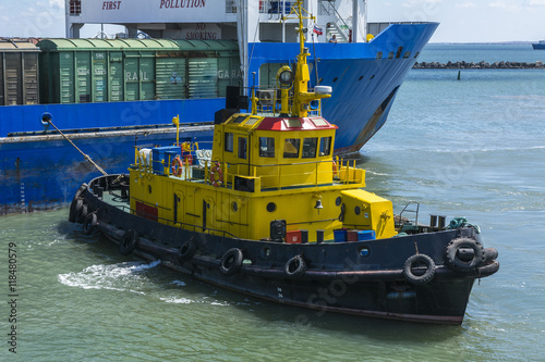 A yellow tugboat assisting a large cargo ship