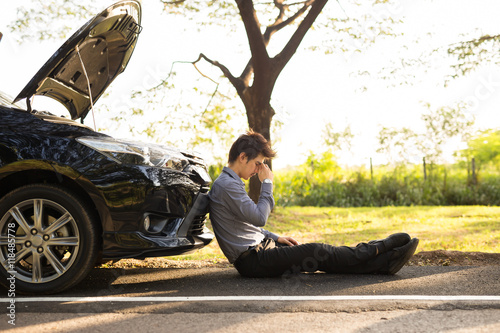 Fotografi Full length of businessman with hands on head sitting by broken down car at coun
