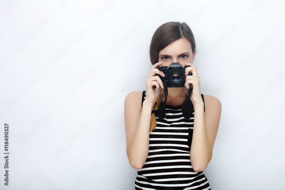 Portrait of happy young beautiful woman in striped shirt posing with black photo camera hiding her face against studio background Portrait of happy young beautiful woman in striped shirt posing with black photo camera hiding her face against studio background