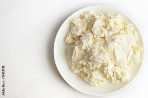Cottage cheese in white saucer on white background.