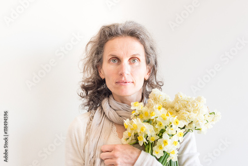 Natural looking middle aged woman with grey hair holding erlicheer daffodils and jonquils