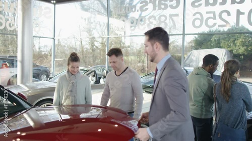 Salesman in car dealership with couple, showing them the engine of new car photo