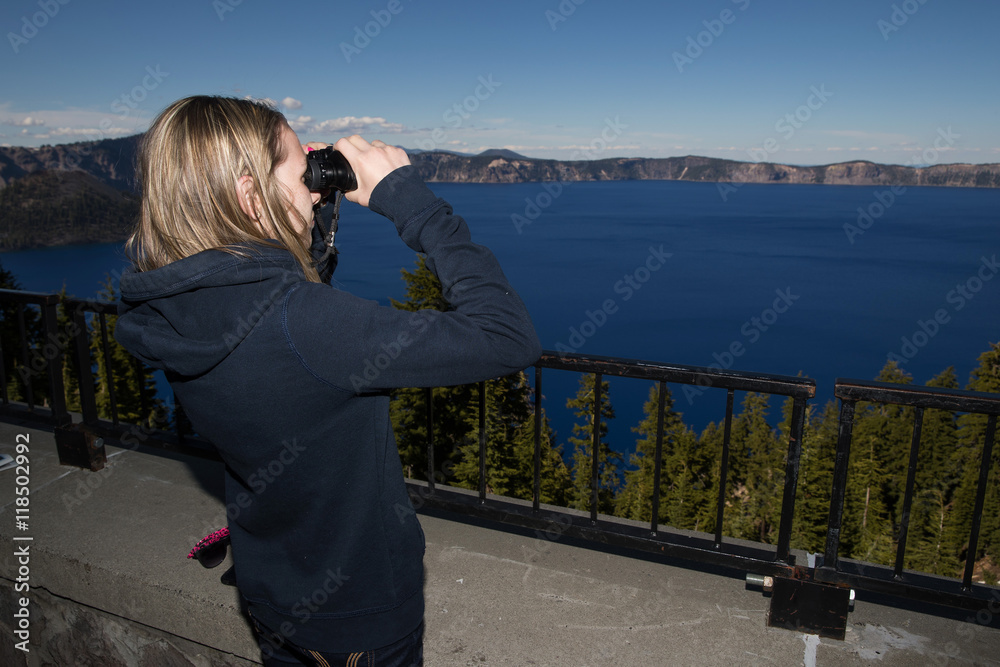 Young girl looking through binoculars at Crater Lake in Oregon,
