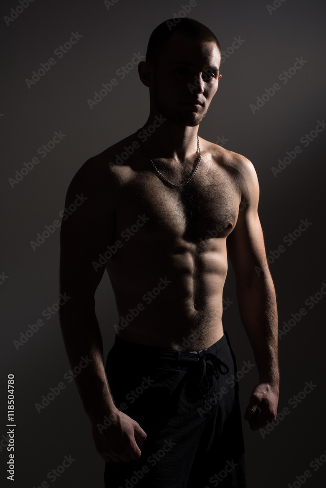 Young man with a naked torso standing in the studio on a gray background. An athlete with a beautiful body