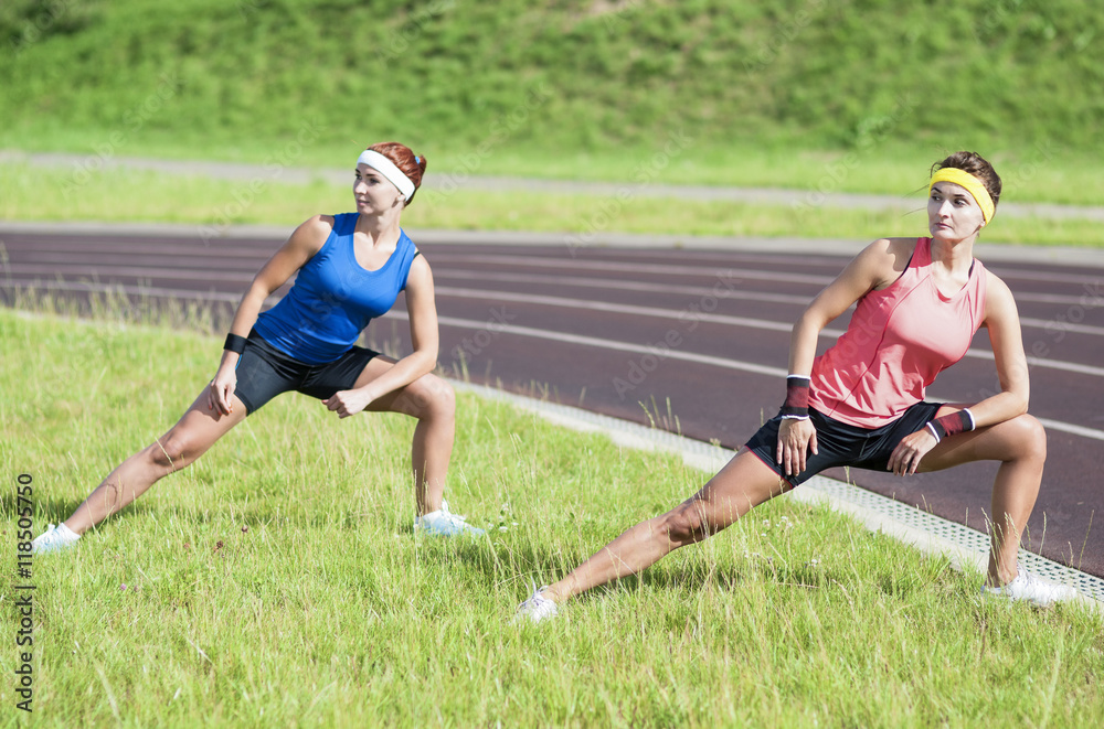 Healthy Lifestyle Ideas and Concepts. Two Young Caucasian Girlfriends Having Trunk Bending Exercises Outdoors Healthy Lifestyle Ideas and Concepts. Two Young Caucasian Girlfriends Having Trunk Bending Exercises Outdoors