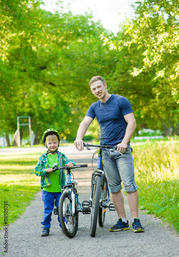 portrait of a happy family - father and son bicycling in the par