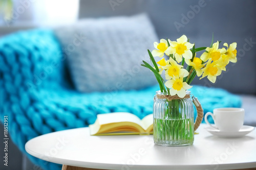 Yellow narcissus on white table in room interior