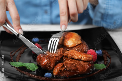 Woman eating juicy meat with sweet sauce in restaurant