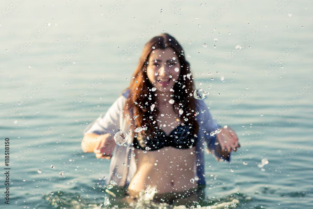 Beautiful young girl splashing the water in the sea