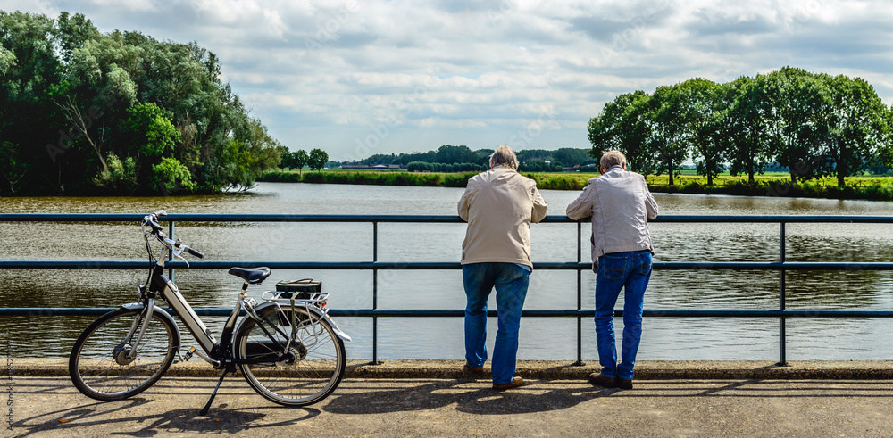 Two elderly men leaning over a bridge railing