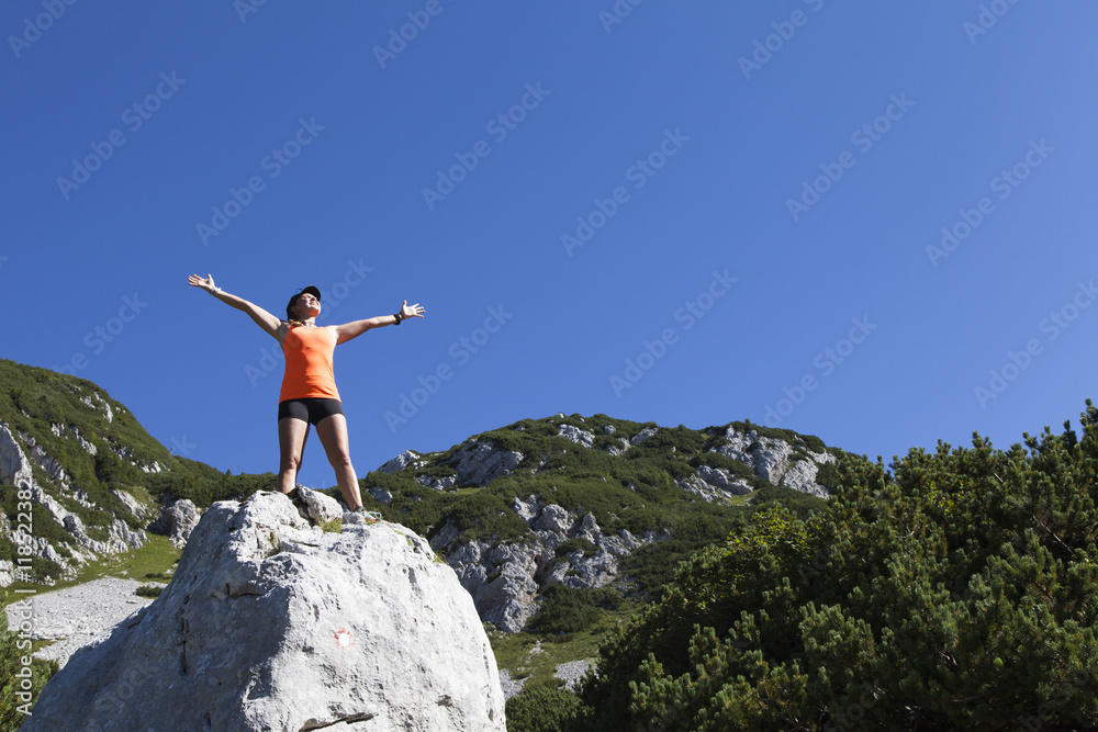 Young pretty smiling woman hiker standing on a rock with raised outstretched hands, high in the mountains, freedom and happiness, achievement in mountains Young pretty smiling woman hiker standing on a rock with raised outstretched hands, high in the mountains, freedom and happiness, achievement in mountains