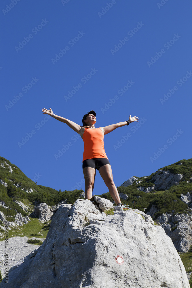Young pretty smiling woman hiker standing on a rock with raised outstretched hands, high in the mountains, freedom and happiness, achievement in mountains Young pretty smiling woman hiker standing on a rock with raised outstretched hands, high in the mountains, freedom and happiness, achievement in mountains