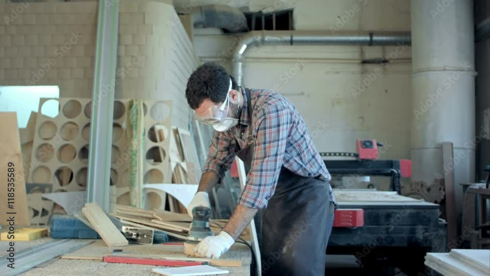 Bearded carpenter in safety glasses working with electric planer in workshop. Bearded carpenter in safety glasses working with electric planer in workshop.