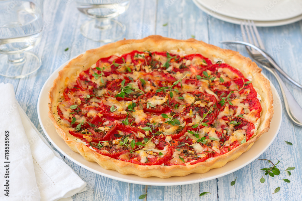 Delicious tomato tart with goat cheese, thyme and garlic on blue wooden table Delicious tomato tart with goat cheese, thyme and garlic on blue wooden table