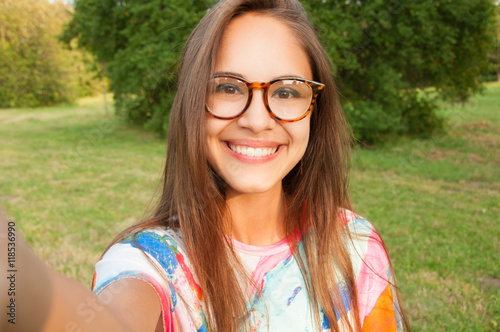 Close up portrait of a young attractive woman holding a smartphone and taking a selfie photo