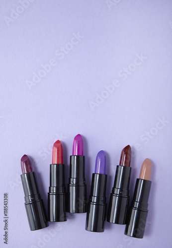 Aerial view of assorted lip stick make up on a pastel purple background forming a page footer