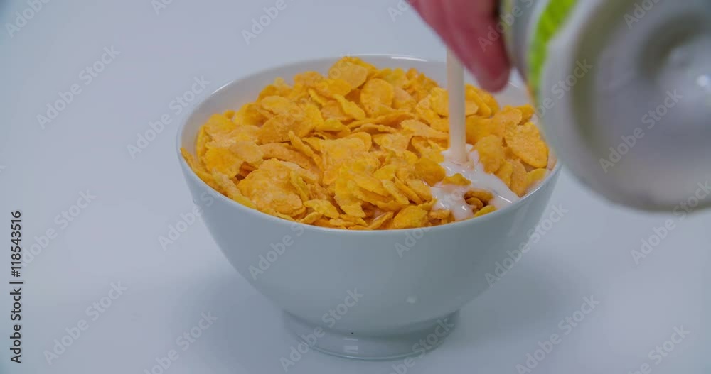A bowl of corn flakes is standing on a table and someone starts pouring some milk into it. Close-up shot.
A bowl of corn flakes is standing on a table and someone starts pouring some milk into it. Close-up shot.