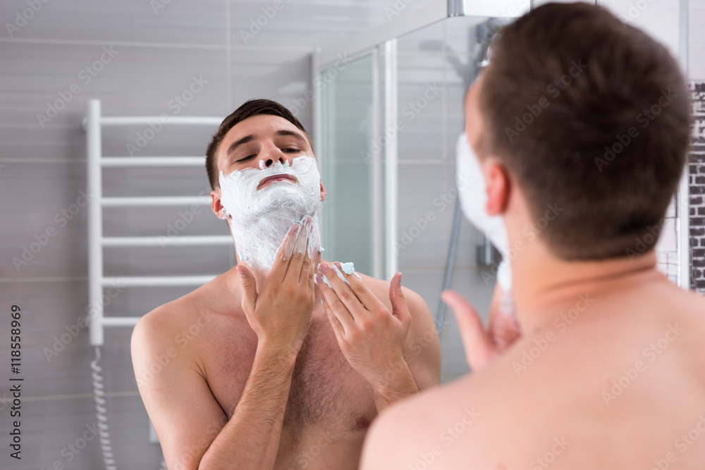 Young man smearing shaving gel on his face