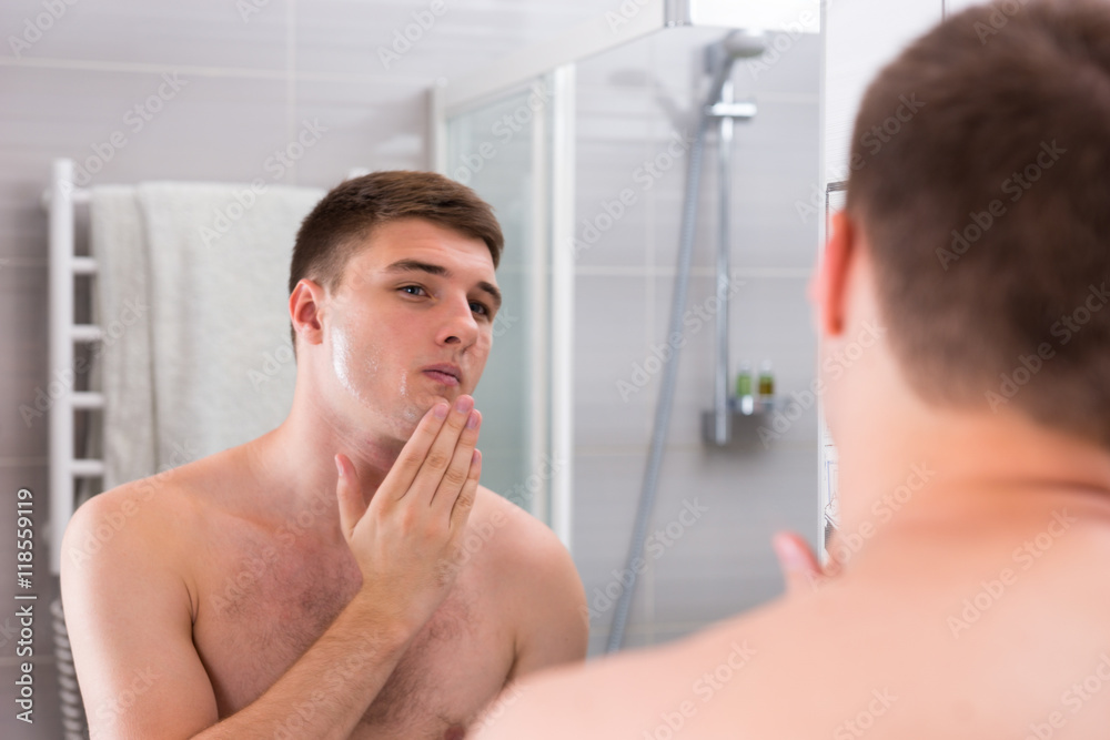 Young man put some aftershave lotion on a face standing in front