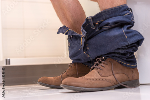 Close up view of male wearing jeans and shoes sitting on the toi
