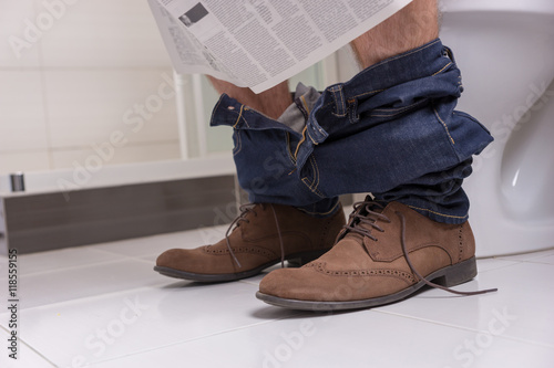 Close up view of male reading newspaper while sitting on the toi