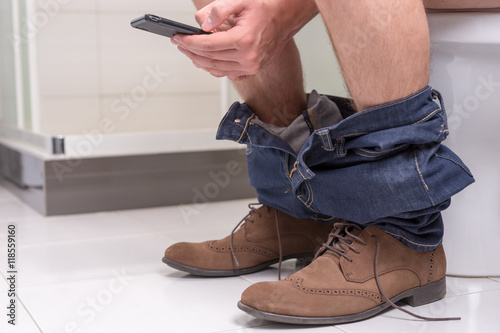 Male using phone while sitting on a toilet bowl