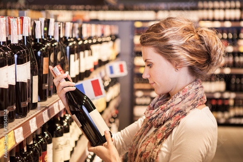 Obraz na plátně Woman trying to decide which bottle of wine to buy