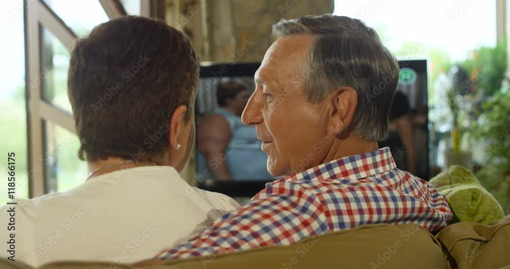Back view of senior couple laughing and talking while watching TV Back view of senior couple laughing and talking while watching TV
