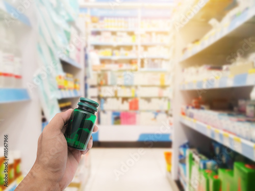 Hand with pill bottle on blurred pharmacy store