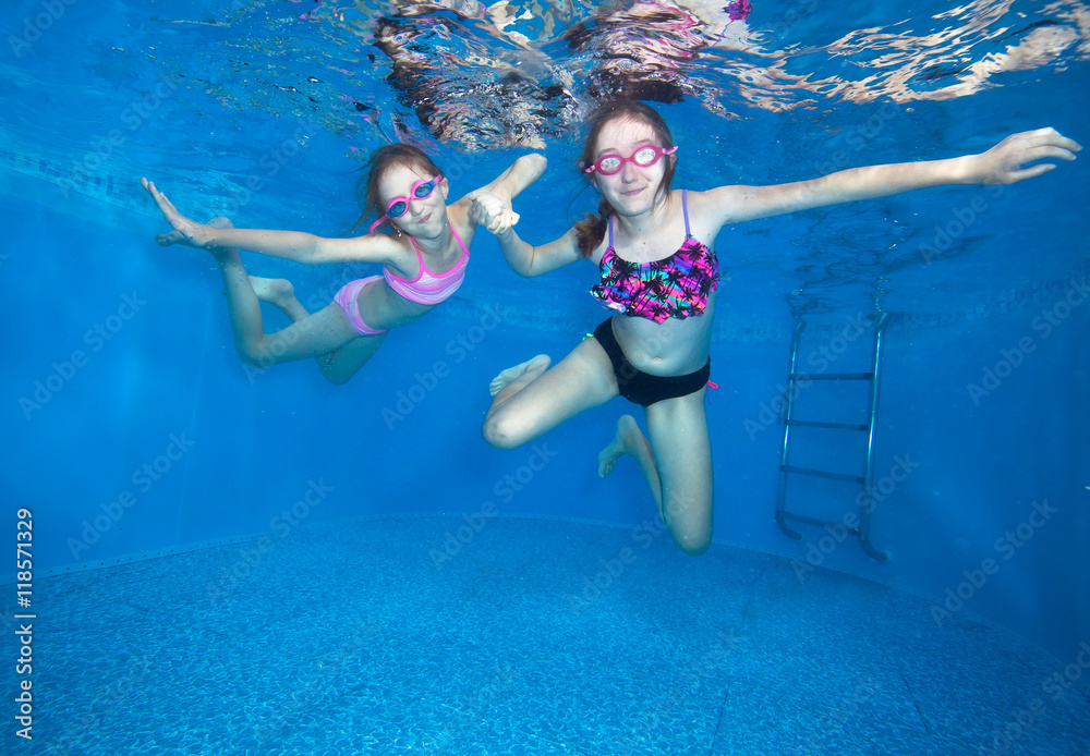 Happy girls swim underwater in pool and having fun, children on summer vacation.