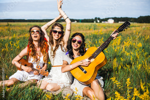 Canvas Print Three cute hippie girl sitting on grass outdoors, best friends having fun and la