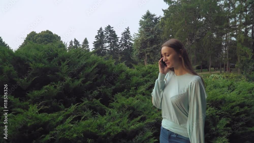 A young girl goes green summer park and talking on the phone, smiles, rejoicing. A young girl goes green summer park and talking on the phone, smiles, rejoicing.