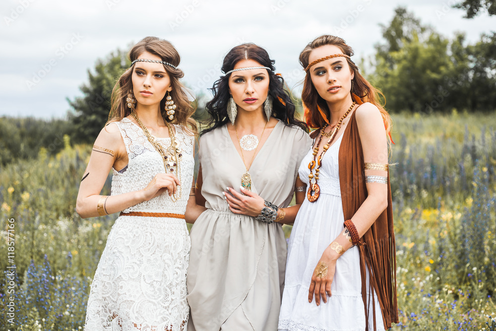 Three beautiful cheerful hippie girls, best friends, the outdoors, cute  smile, trendy hairstyles, feathers in her hair, white dress, tattoo flash,  gold accessories, Bohemian, boho style, fashion indie foto de Stock