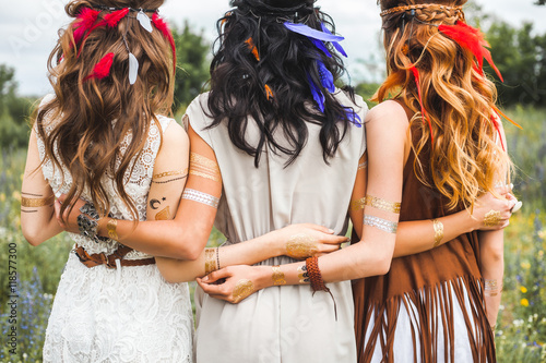Three beautiful cheerful hippie girls, best friends, the outdoors, cute smile, trendy hairstyles, feathers in her hair, white dress, tattoo flash, gold accessories, Bohemian, boho style, fashion indie photo