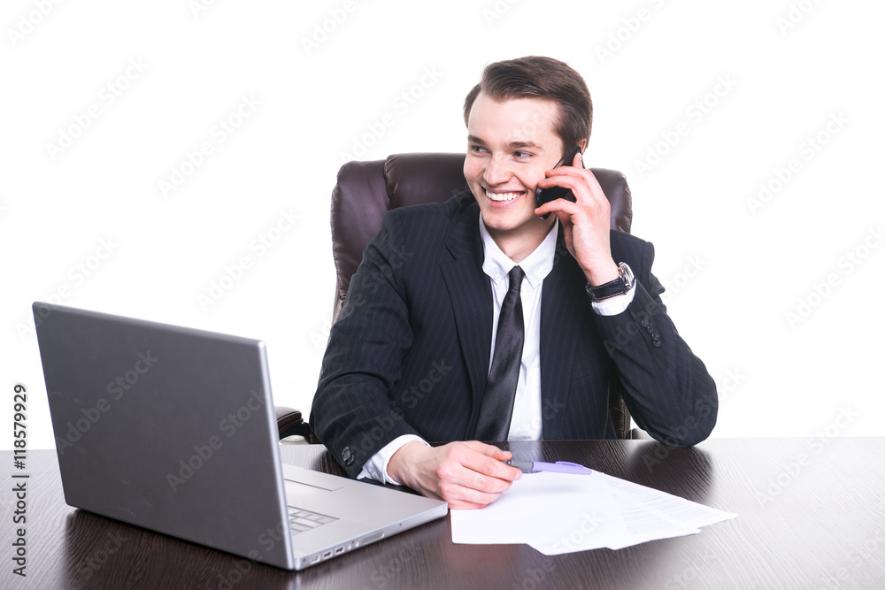 Young smiling businessman working at the office on laptop, talks on cell phone and smiling. Young smiling businessman working at the office on laptop, talks on cell phone and smiling.