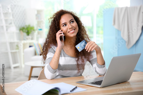 Beautiful young woman using credit card and phone for online shopping