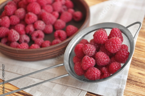 Fresh raspberry in sieve and plate, closeup photo