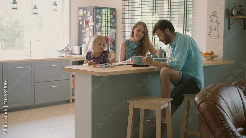 Happy wife is talking to her husband and fixing her daughters hair at the kitchen table. Slow motion Happy wife is talking to her husband and fixing her daughters hair at the kitchen table. Slow motion