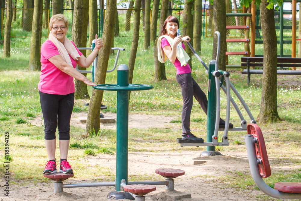 Senior and young woman exercising upper and lower body on outdoor gym, healthy lifestyle