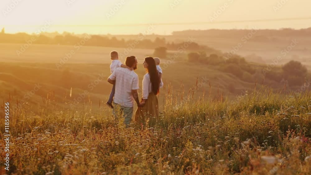 Happy family at sunset. Standing on a hill against the setting sun, holding their two children Happy family at sunset. Standing on a hill against the setting sun, holding their two children