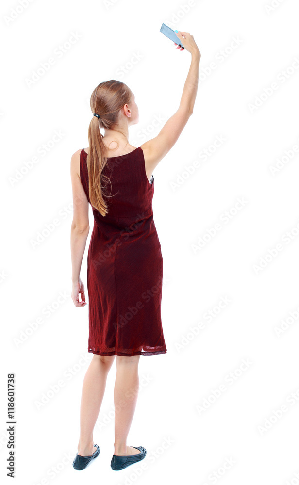 Fototapeta premium back view of standing young beautiful woman using a mobile phone. girl watching. Rear view people collection. backside view of person. Isolated over white background. The girl in the maroon