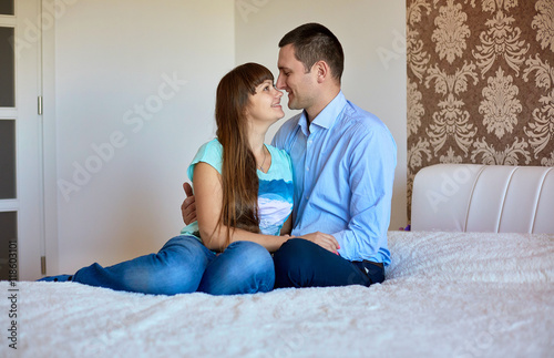 Smiling family couple sits on the bed hugging each other