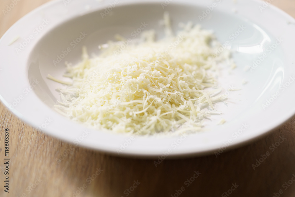 grated parmigiano in white plate over wood table grated parmigiano in white plate over wood table