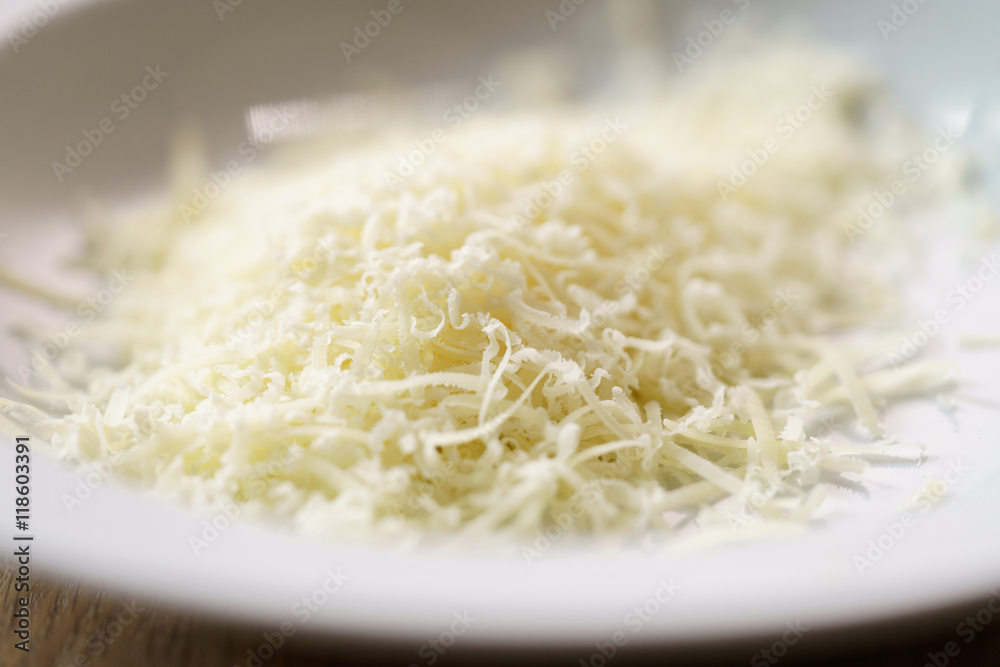grated parmigiano in white plate over wood table grated parmigiano in white plate over wood table