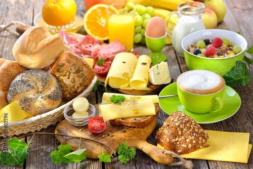 Rustikaler, bunter Frühstückstisch mit Käseröllchen und weiterer reichlicher Auswahl - Outside served colorful breakfast with a large selection of food and a cup of cappuccino 