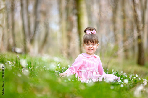 Beautiful child in pink dress sits on the flower glade
