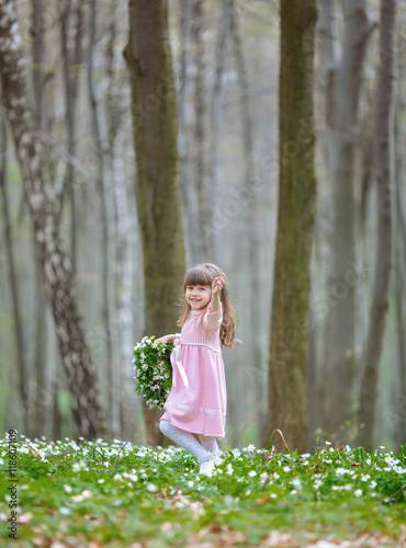 Child shakes her hand while standing on the glade with wreathe