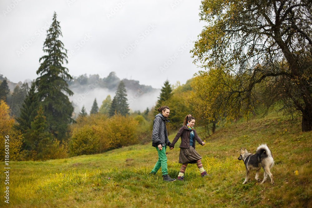 Happu couple walks to the dog standing on green hill