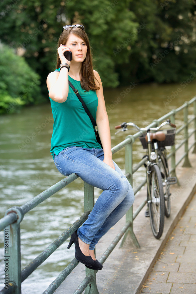 young woman sitting by river and talking on phone